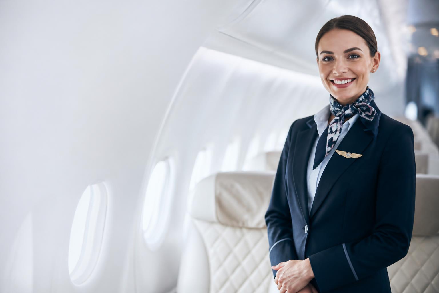 Smiling flight attendant in uniform standing confidently inside a bright, luxurious airplane cabin